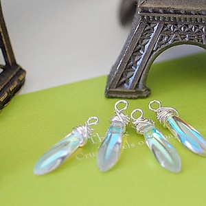 Puede incluir: Cuatro colgantes de cristal iridiscente con alambre de plata. Los cristales en forma de lágrima reflejan un arcoíris de colores. Los colgantes están sobre una superficie verde, con una Torre Eiffel en miniatura en el fondo.