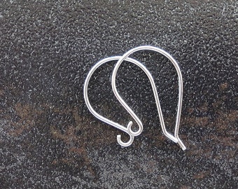 May include: A pair of silver earring hooks, also known as ear wires, are shown on a dark gray textured surface. The hooks are made of metal and have a simple, classic design.
