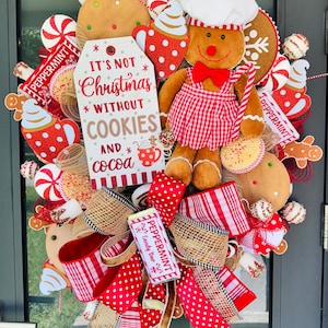 Puede incluir: Una corona navide&ntilde;a festiva con un hombre de jengibre, mentas y galletas. La corona incluye cintas rojas y blancas, un letrero que dice "It's not Christmas without cookies and cocoa" y una barra de caramelo de menta.