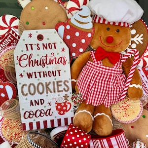 Puede incluir: Una corona navide&ntilde;a festiva con un hombre de jengibre con gorro y delantal de chef, sosteniendo un bast&oacute;n de caramelo. La corona incluye galletas de jengibre, mentas y un letrero que dice "It's not Christmas without cookies and cocoa."
