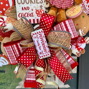 Puede incluir: Una corona navide&ntilde;a festiva con cintas de lunares y cuadros rojos y blancos, arpillera y una barra de caramelo de menta. La corona incluye un letrero que dice "Sin galletas y cacao". Tambi&eacute;n se ven hombres de jengibre y bastones de caramelo.