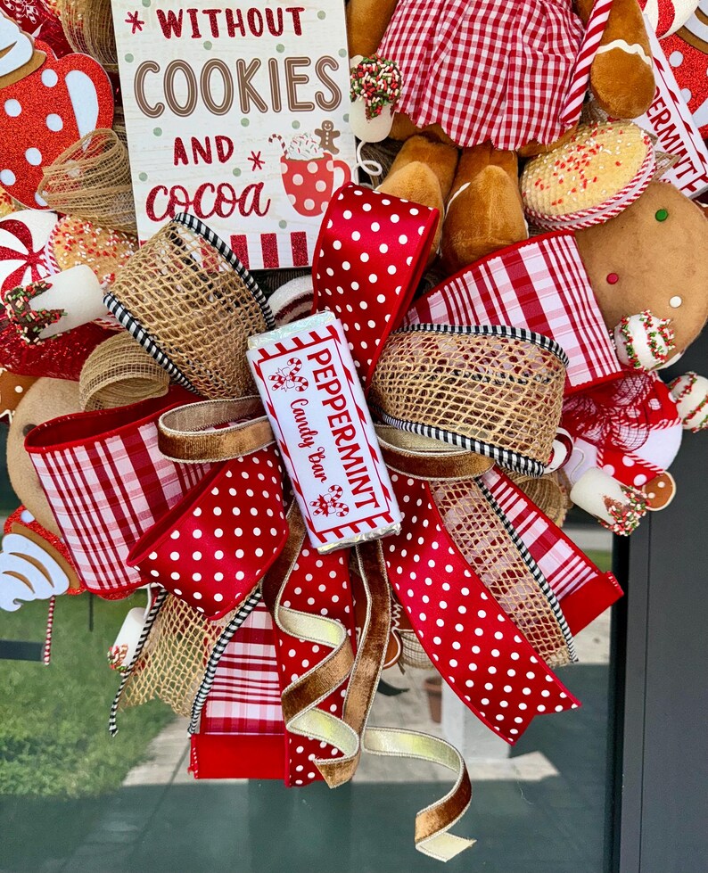 Puede incluir: Una corona navide&ntilde;a festiva con cintas de lunares y cuadros rojos y blancos, arpillera y una barra de caramelo de menta. La corona incluye un letrero que dice "Sin galletas y cacao". Tambi&eacute;n se ven hombres de jengibre y bastones de caramelo.