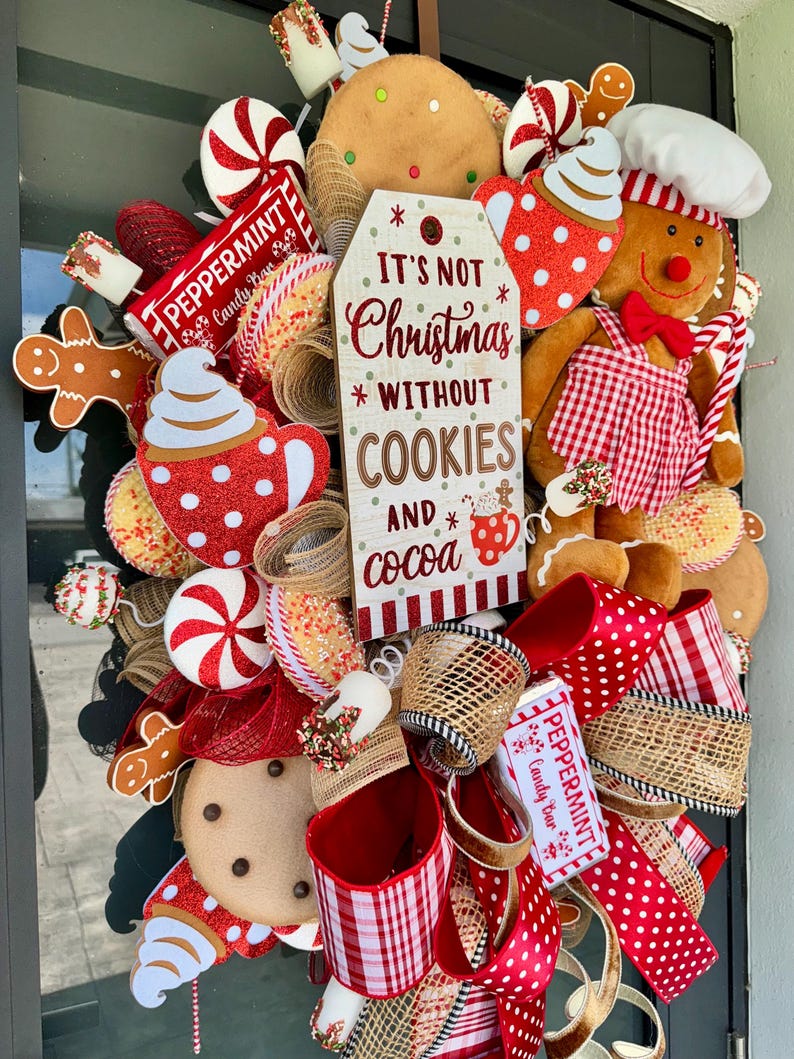 Puede incluir: Una corona navide&ntilde;a festiva con hombres de jengibre, galletas, caramelos de menta y cintas rojas y blancas con lunares. La corona incluye un letrero que dice "It's Not Christmas Without Cookies and Cocoa."