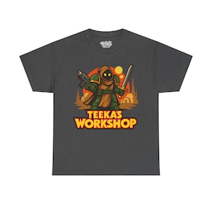 Puede incluir: Camiseta gris oscuro con un guerrero de dibujos animados que sostiene un bláster y una espada, vestido con una capa con capucha y una armadura. El texto "TEEKA'S WORKSHOP" está en amarillo y naranja. La camiseta tiene cuello redondo y mangas cortas.