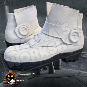 Puede incluir: Un par de botas de cuero blanco con suelas negras y una correa alrededor del tobillo. Las botas tienen una hebilla circular en el lateral.