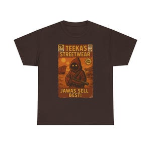 Puede incluir: Camiseta marrón con un gráfico retro. El diseño presenta el texto "Teeeka's Streetwear" y "Jawas Sell Best!" junto con una ilustración de un personaje Jawa. El gráfico tiene un estilo de cómic vintage, con una combinación de colores marrón y naranja.
