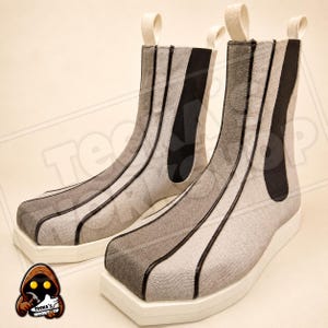Pode incluir: Um par de botas de cano curto com cabedal em tecido texturizado cinza claro e detalhes em debrum preto vertical. As botas possuem bico quadrado, sola plataforma branca espessa e uma aba de puxar branca no calcanhar. Painel lateral elástico.