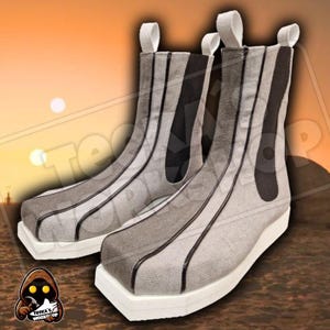 Op de afbeelding: Een paar enkellaarsjes met een uniek design. De laarzen hebben een lichtgrijze stof met verticale donkergrijze en zwarte accenten. Ze hebben witte zolen en treklussen. De laarzen zijn ontworpen met een futuristische esthetiek.