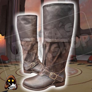 Peut inclure: Paire de bottes en cuir marron avec boucles. Les bottes ont une tige haute et un dessus replié. Elles sont faites d'une combinaison de cuir lisse et de type daim. Bottes de couleur marron foncé, pour cosplay ou costume.