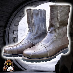 May include: A pair of brown leather boots with white stitching and a black sole. The boots are mid-calf length and have a zip closure. The boots are set against a blurred background.