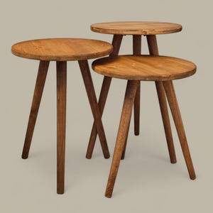 Può includere: Set di tre tavolini in legno. Ogni tavolo ha un piano rotondo e tre gambe angolate. I tavoli sono realizzati in legno marrone chiaro e variano leggermente in altezza. Design semplice e moderno.