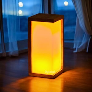May include: A square wooden lamp with a warm orange glow. The lamp is made from natural wood and has a simple, modern design.