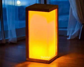 May include: A wooden lamp with a square shape and a warm orange glow. The lamp is made of natural wood and has a simple, modern design.