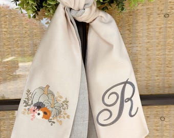 Può includere: Sciarpa per porta in tessuto beige con finiture grigie e beige, annodata. Un lato presenta un disegno ricamato di zucche e fiori. L'altro lato mostra una lettera "R" corsiva grigia.