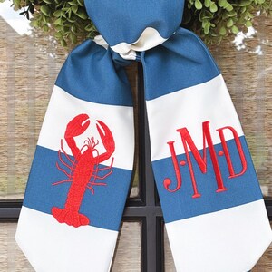 May include: A blue and white striped fabric bow with a red lobster on one side and the monogram "JMD" on the other side.