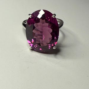 May include: A silver ring with a large, oval-shaped, purple gemstone.