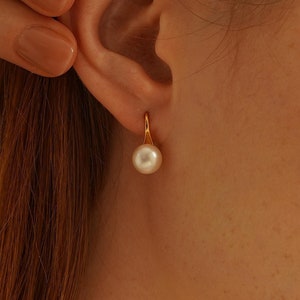 May include: A pair of gold hoop earrings with a single white pearl dangling from each hoop.