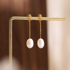 Puede incluir: Un par de pendientes de oro con una sola perla blanca en cada pendiente.