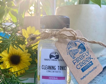 May include: A small clear glass bottle with a black lid, containing a cleaning tonic concentrate. The bottle is labeled "Firefly Creek Tonics Cleaning Tonic Concentrate Herbal Net Wt. 4 oz. (Makes 16 oz.)". The bottle is tied with twine and a brown paper tag that reads "Earth Derived & Made with Love in NC. Firefly Creek Tonics FireflyCreekTonics.Etsy.com".