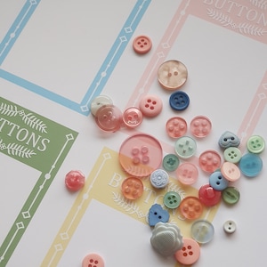 Pode incluir: Uma coleção de botões coloridos em vários formatos e tamanhos, incluindo botões em forma de coração, redondos e quadrados. Os botões estão dispostos em uma superfície branca com fundos amarelos, rosa e verdes. O texto "BUTTONS" é visível no fundo.