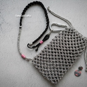 May include: A gray macrame phone pouch with a silver carabiner and a matching lanyard. The lanyard is black and gray with pink accents. The image also includes a pair of earrings and the text "kenatastudio".