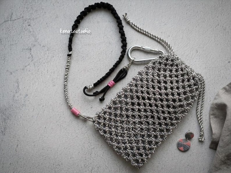 May include: A gray macrame phone pouch with a silver carabiner and a matching lanyard. The lanyard is black and gray with pink accents. The image also includes a pair of earrings and the text "kenatastudio".