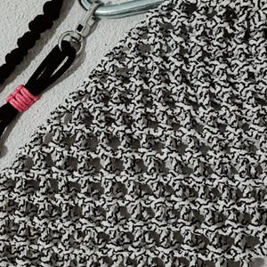 May include: A macrame phone case in black and white, attached to a silver carabiner clip. A black cord with a pink accent and a black cord are also visible. The brand name "kenatastudio" is in the upper left corner.