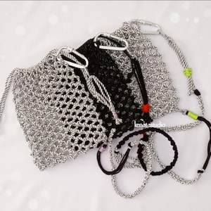 May include: A collection of handmade macrame bags and bracelets in black and silver. The bags feature a drawstring closure and carabiner clips. The bracelets are black and silver, with a variety of cord designs. The bags and bracelets are displayed on a white surface.