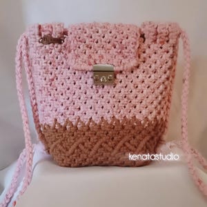May include: A handmade pink and brown crochet bag with a flap closure and a silver clasp. The bag has a braided strap and a textured design. The bottom of the bag is a darker brown colour. The text "kenatastudio" is visible on the bottom right.