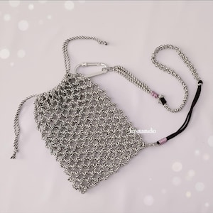 May include: A black and white woven pouch with a drawstring closure and a silver carabiner clip. The pouch has a matching lanyard with a black cord and pink beads. The pouch is designed to hold a phone or other small items.