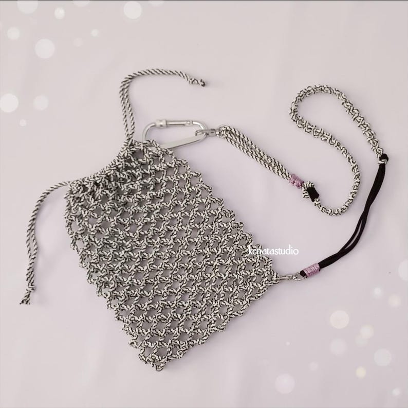 May include: A black and white woven pouch with a drawstring closure and a silver carabiner clip. The pouch has a matching lanyard with a black cord and pink beads. The pouch is designed to hold a phone or other small items.