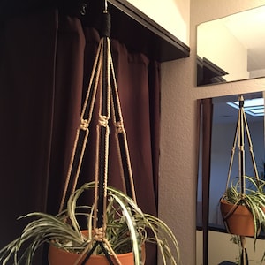 May include: A hanging plant holder made of black and natural colored rope with a plant in a terracotta pot.