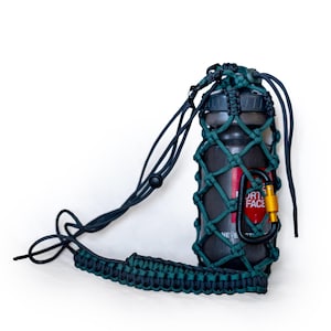 May include: A dark water bottle with a red and white logo is held in a green and black woven carrier. The carrier has a black strap and a gold carabiner clip. The bottle is designed for outdoor activities.
