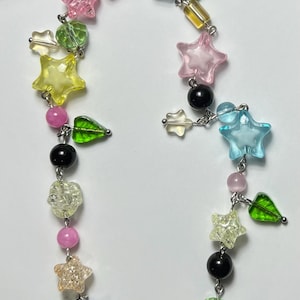 May include: A colorful beaded necklace featuring star, leaf, and round beads in various colors including pink, yellow, green, and blue. The necklace is strung on a silver chain with a pink cord for hanging.