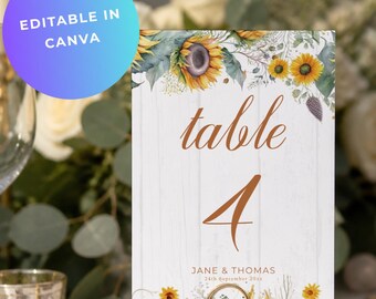 May include: A rectangular table number card featuring a white wood grain background, decorated with watercolor sunflowers and greenery. The text reads "table 4" in a copper script font, followed by "JANE & THOMAS" and "24th September 20xx".