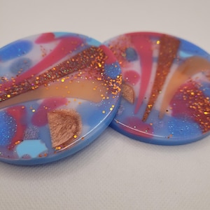 May include: Two round blue resin coasters with a white, pink, and orange marbled design and gold glitter accents.