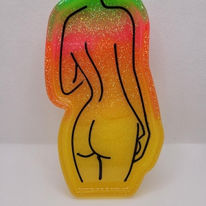 May include: A colorful resin tray with a glittery finish. The tray features a black outline of a person's back and buttocks. The colors transition from green to orange to yellow.