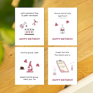 May include: Four white birthday cards with science-themed illustrations and text. Each card features a different design with lab equipment, molecules, and the phrase "Happy Birthday." The cards have humorous science-related messages.