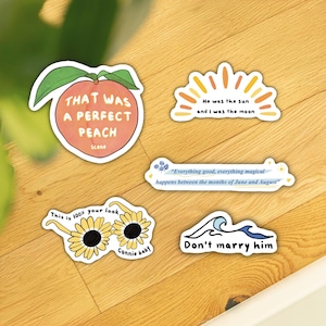 Pu&ograve; includere: Una collezione di adesivi bianchi con vari disegni e testo. Un adesivo &egrave; una pesca con la scritta "THAT WAS A PERFECT PEACH Scene". Altri adesivi includono frasi come "He was the sun and I was the moon" e "Don't marry him".