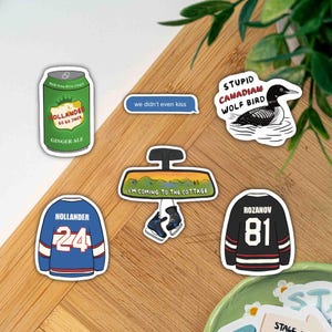 May include: A selection of stickers with diverse designs. Includes a green ginger ale can, a blue speech bubble with text, a black and white bird, a hockey jersey with the name "HOLLANDER" and the number "24", a car mirror with text, and a hockey jersey with the name "ROZANOV" and the number "81".