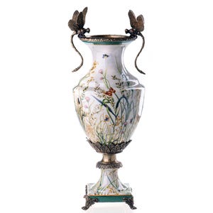 Op de afbeelding: Een witte keramische vaas met een bloemenmotief en gouden accenten. De vaas heeft twee libellenhandvatten en staat op een vierkante voet met gouden poten.