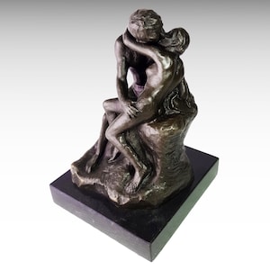 May include: A bronze sculpture of two figures embracing and kissing. The sculpture is mounted on a black marble base.