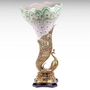 Könnte beinhalten: Eine dekorative Vase mit einer weißen Keramikschale, die mit einem grün-weißen Pfauenfeder-Muster verziert ist. Der Sockel besteht aus goldfarbenem Metall in Form eines Pfaus mit filigranen Details und steht auf einem schwarzen Fuß.