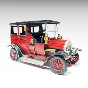 Peut inclure: Modèle réduit de voiture ancienne en métal rouge avec des détails noirs. La voiture ancienne a un toit noir, des phares dorés et des roues rouges. La voiture miniature présente un intérieur détaillé et se détache sur un fond blanc.