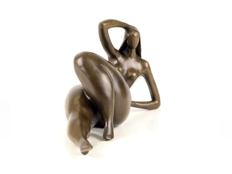 May include: A bronze sculpture of a reclining nude figure. The figure is posed with one arm raised above their head and the other arm resting on their thigh. The sculpture is made in a realistic style.