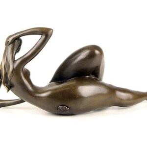 May include: Bronze sculpture of a reclining nude figure. The figure is posed with one arm raised above the head and the other arm resting on the hip. The sculpture is finished in a dark brown patina.