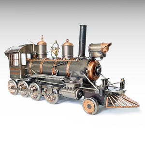 Könnte beinhalten: Ein Dampflokomotiv-Modell aus Metall mit dunkelgrauem Körper und kupferfarbenen Akzenten an den Rädern, Kesselringen und Domen. Die Lokomotive verfügt über einen hohen schwarzen Schornstein, eine kleine Glocke, einen Kuhfänger und einen Scheinwerfer.