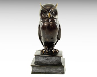 May include: A bronze owl sculpture perched on a stack of books. The owl has a detailed, realistic design with sharp eyes and a fierce expression.