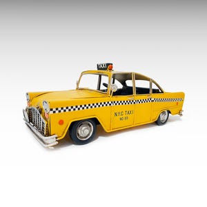 May include: A yellow metal model car designed as a New York City taxi. The vehicle features a black and white checkered stripe along the side, a roof-mounted taxi sign, and the text N.Y.C TAXI NO. 69 printed on the door. It has silver-colored bumpers.