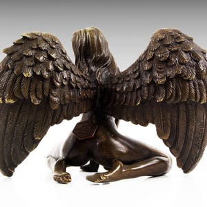 Puede incluir: Escultura de bronce de una figura alada con las alas extendidas. La figura est&aacute; arrodillada con la cabeza girada hacia un lado. La escultura est&aacute; firmada "J. Patou" en el ala derecha.